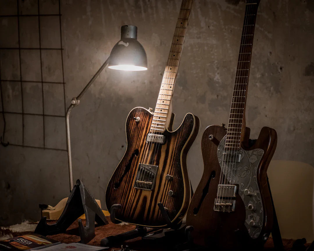 Two high-end electric guitars with wood finishes under a desk lamp in a rustic setting