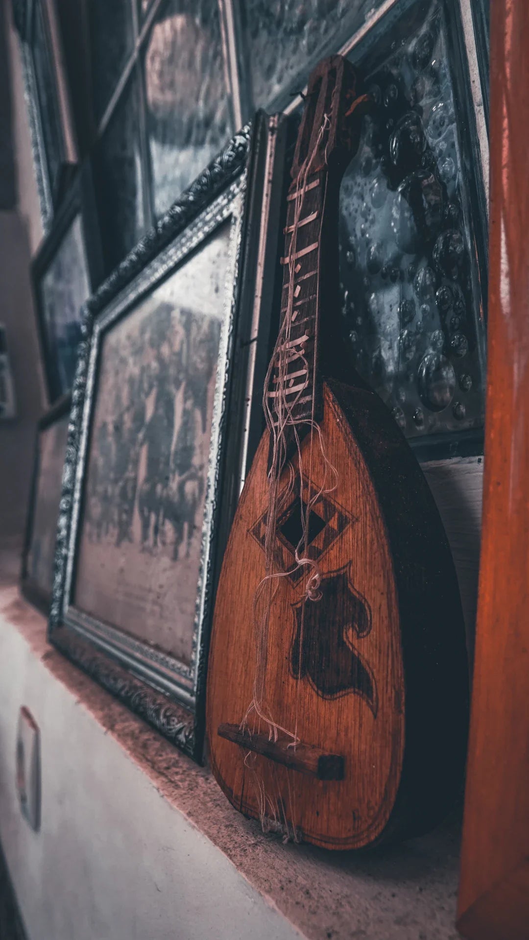 Vintage wooden stringed instrument with ornate designs, resting against framed photos