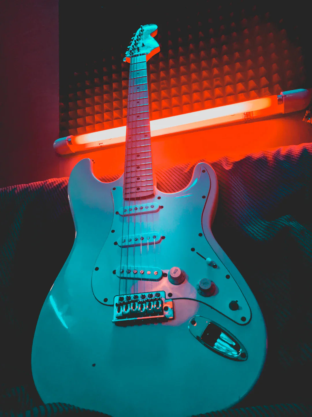 Electric guitar with white body and maple neck in colorful studio lighting