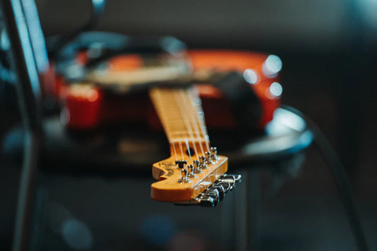 Close-up of electric guitar headstock and neck with a blurred red guitar body in the background