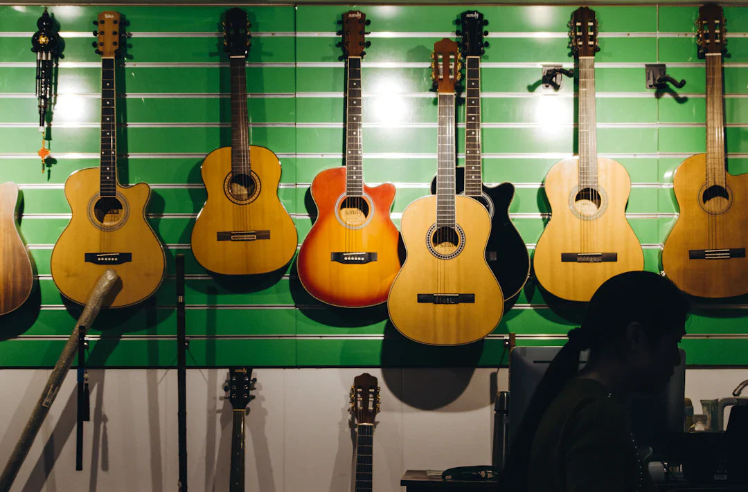 Various acoustic guitars hanging on a green wall in a guitar shop showroom