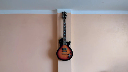 Sunburst electric guitar hanging on a peach-colored wall indoors